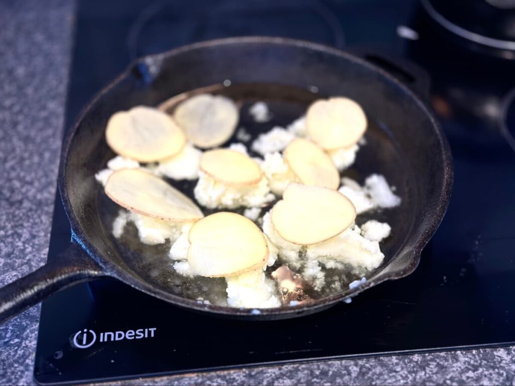 Slices of potato on to of solid beef tallow in a cast iron pan