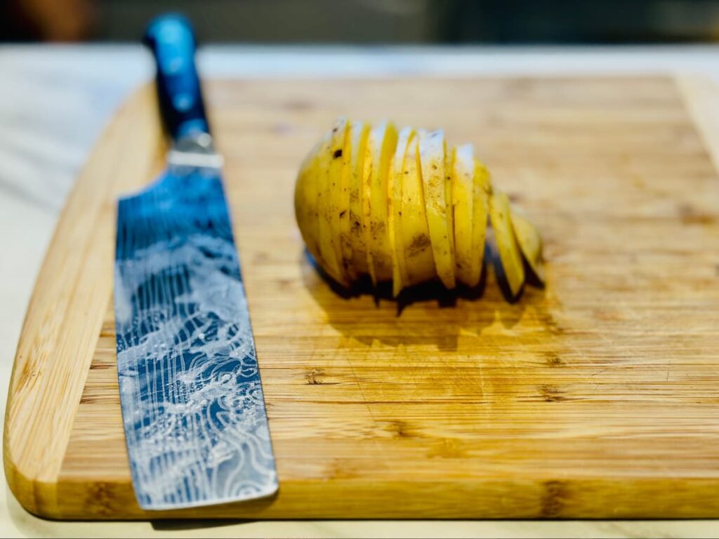 A sliced potato on a chopping board, beside a large knife