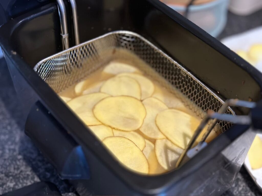 Slices of potato on top of solid fat in a deep fat fryer
